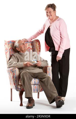 Anziani: Cura e attenzione. Una moglie attenta che si prende cura del marito seduto. Ritratto a lunghezza intera, isolato su bianco. Da una serie. Foto Stock