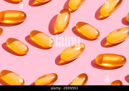 Composizione di pillole di vitamina arancione sparse su sfondo rosa in studio luce Foto Stock
