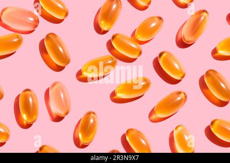 Composizione di pillole di vitamina arancione sparse su sfondo rosa in studio luce Foto Stock