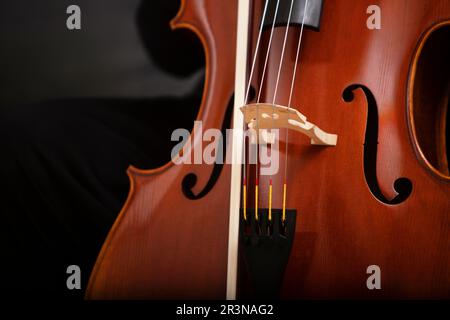 Primo piano di violoncello classico in legno con archi metallici e parte in legno marrone lucido con arco posto su sfondo scuro in studio Foto Stock