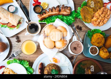 Vista dall'alto di appetitosi piatti colombiani con papas rellenas pan de bono chicharron bunuelos e caldo de costilla con varie bevande servite Foto Stock