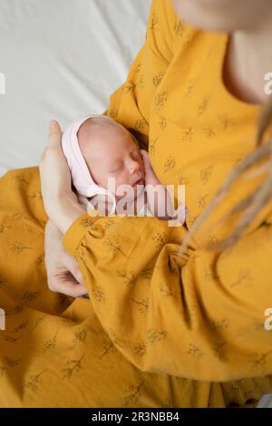 Dall'alto donna senza volto in abito giallo rilassante su un comodo letto e tenendo adorabile bambino dormire in pace con gli occhi chiusi nelle mani Foto Stock