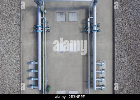 Alto angolo di costruzione di tubazioni e tubi metallici con pompe di circolazione e valvole con tubo verde vicino ai portelli delle fognature Foto Stock