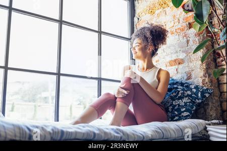 Ragazza rilassata afro-americana compiaciuta di etnia in casa seduta sul davanzale Foto Stock