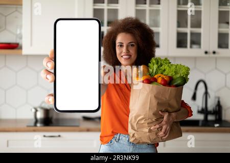 App per la consegna di alimentari Donna nera con smartphone vuoto e borsa con prodotti alimentari Foto Stock