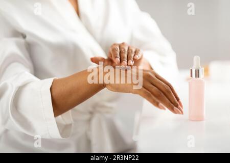 Idratante per la pelle. Donna nera che applica il siero nutriente sulle mani nel paese Foto Stock