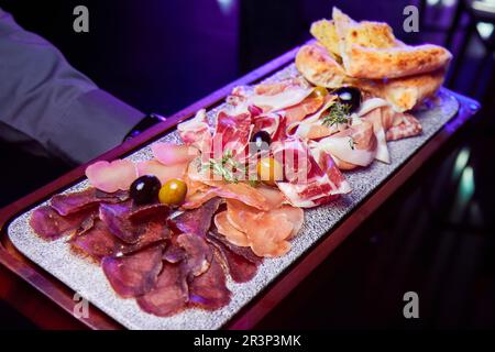 Il cameriere tiene un piatto di legno con varie prelibatezze a fette di carne secca Foto Stock