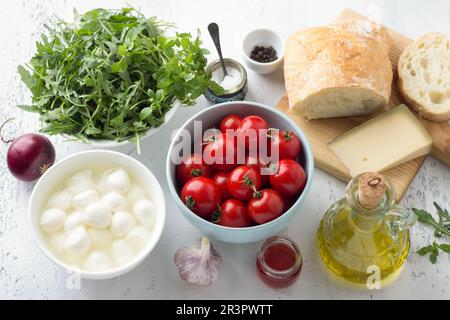 Ingredienti per l'insalata di panzanella italiana: Pomodori ciliegini, rucola, basilico, mozzarella, pane di ciabatta, parmigiano, olio d'oliva, cipolla rossa, aglio, Foto Stock