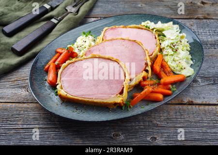 Bistecca di maiale Kasseler in crosta di pasta sfoglia con cavolo e carote savoy servita come primo piano su un piatto di design nordico Foto Stock