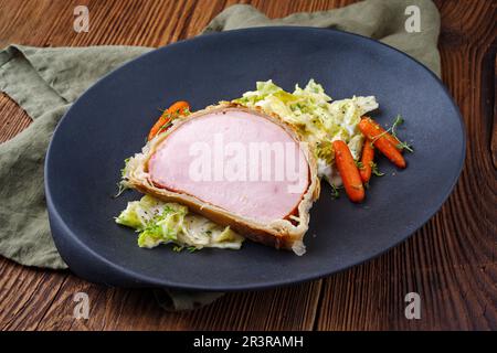 Bistecca di maiale Kasseler in crosta di pasta sfoglia con cavolo e carote savoiarda servito come primo piano su un piatto di design Foto Stock