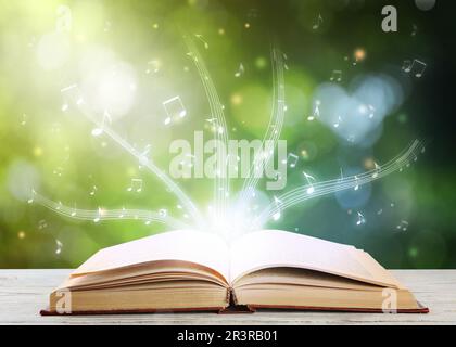 Musica che scorre dal libro. Simboli musicali che volano su tome su un tavolo di legno bianco su sfondo sfocato Foto Stock