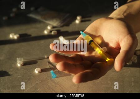 Dipendente uomo che tiene siringa vicino a farmaci a tabella testurizzata grigia, primo piano Foto Stock