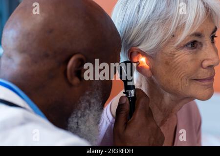 Diverso medico di sesso maschile senior utilizzando otoscopio esame orecchio di sorridente paziente di sesso femminile senior, copia spazio Foto Stock