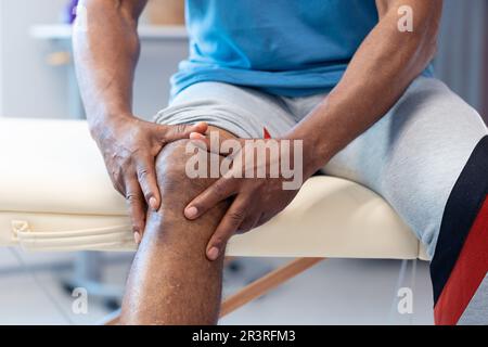 Sezione centrale del paziente di sesso maschile africano americano anziano che tiene il ginocchio nella sessione di fisioterapia, spazio copia Foto Stock