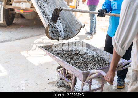 I lavoratori caricano calcestruzzo dai camion al carrello per versare il pavimento all'interno. Cantiere. Foto Stock