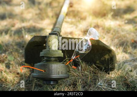 Rifinitore dopo la falciatura dell'erba in primo piano. Pompa benzina sull'erba con occhiali di sicurezza. Paesaggistica e paesaggistica del giardino plo Foto Stock