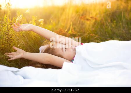 La ragazza dorme sul letto in erba, dolci stirate e sbadigliate sonnolentemente, buon mattino all'aria aperta. Eco-friendly, sonno sano, beneficio Foto Stock