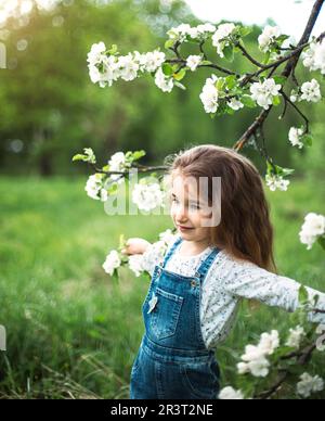 Una bambina carina di 5 anni in un frutteto di mela bianca fiorente in primavera. Primavera, frutteto, fioritura, allergia, primavera f Foto Stock