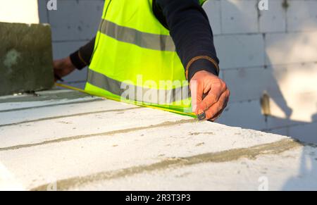 Il lavoratore di costruzione in cantiere misura la lunghezza dell'apertura della finestra e la parete con metro a nastro. Cottage sono m Foto Stock