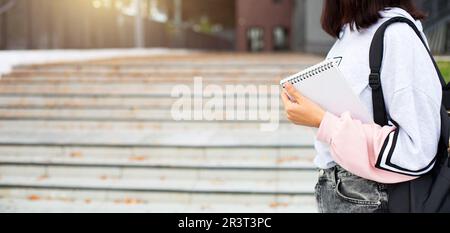 Una studentessa di sesso femminile con uno zaino nero e un notebook in mano si alza sui gradini davanti all'università. Istruzione superiore Foto Stock