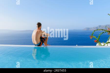 Uomini che si rilassano in piscina durante le vacanze a Santorini Infinity con vista sull'oceano Foto Stock