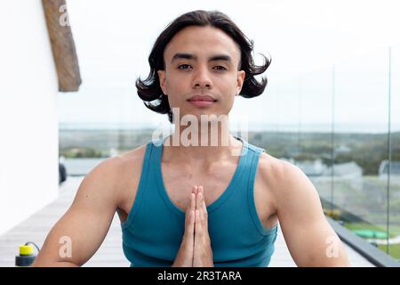 Ritratto di felice uomo biraciale che fa yoga, meditando sul balcone Foto Stock