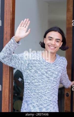 Ritratto di felice uomo biraciale che apre la porta e ondeggiante Foto Stock