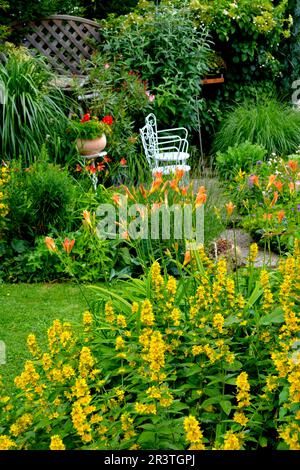 Giardino fiorito in estate, area salotto nel giardino con sedie bianche Foto Stock