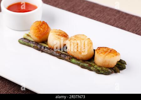 capesante fritte con asparagi su un piatto bianco e salsa Foto Stock