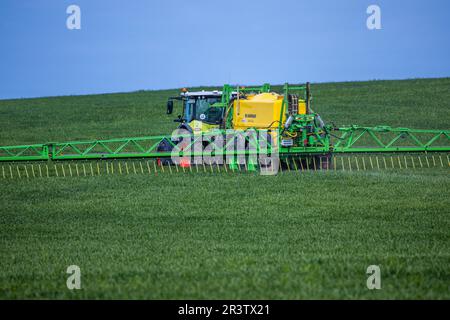 PRODUZIONE - 17 maggio 2023, Meclemburgo-Pomerania occidentale, Kirchdorf (poel): Un trattore traina un'irroratrice con bracci larghi e distribuisce fertilizzanti e pesticidi su un campo di grano. Foto: Jens Büttner/dpa Foto Stock