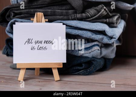 TUTTO CIÒ DI CUI HAI BISOGNO È MENO testo su carta nota su Jeans assortimento abbigliamento shopping sostenibile di seconda mano. Armadio a capsula minimal. Consumo eccessivo di moda sostenibile, consumo di acquisto cosciente, concetto di idea di modo lento. Stile di vita a basso contenuto di rifiuti Foto Stock