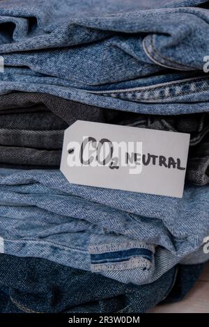 Nota di testo sulle emissioni neutre di CO2 su una pila di jeans. Ecologia natura amichevole, cambiamento climatico, carburante verde e concetto di protezione della terra. Etichetta riciclata con carta per emissioni di carbonio. Abbigliamento naturale biologico jeans con CO2 tag neutro verificato. Foto Stock