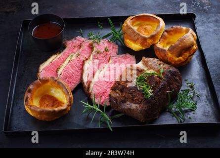 Tradizionale arrosto di manzo della domenica del Commonwealth affettato con budino dello Yorkshire e salsa di vino rosso servito come primo piano su un nero rustico Foto Stock