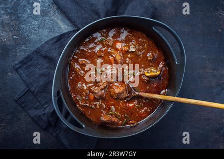 Tradizionale gulasch di cervo brasato ungherese con verdure ed erbe in salsa piccante servito come vista dall'alto in una pentola di stufato di design Foto Stock