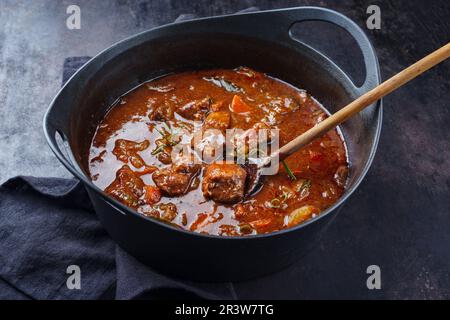 Tradizionale gulasch di cervo brasato ungherese con verdure ed erbe in salsa piccante servito in una pentola di stufato di design Foto Stock