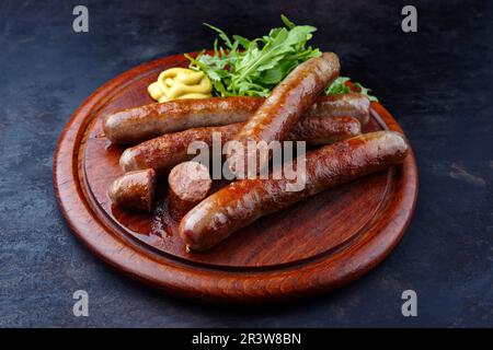 Bratwurst di manzo fritto AllgÃ¤u wagyu con senape calda e lattuga razzo servito da primo piano su un tagliere rustico in legno Foto Stock