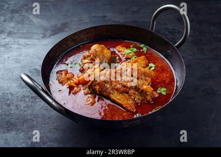 Tradizionale pollo indiano speziato Madras curry Rogan Josh con bacchette e ali serviti come primo piano in una ciotola korei Foto Stock