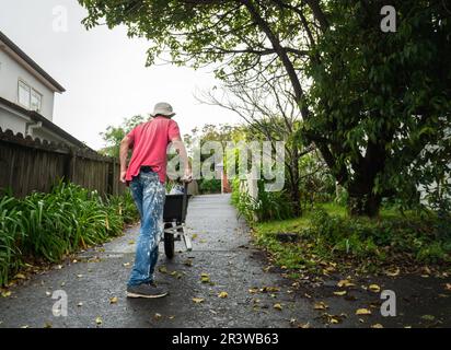 Un uomo che spinge una carriola piena di lattine di vernice sul vialetto di accesso in cemento. Home ristrutturazione fai da te progetto. Foto Stock