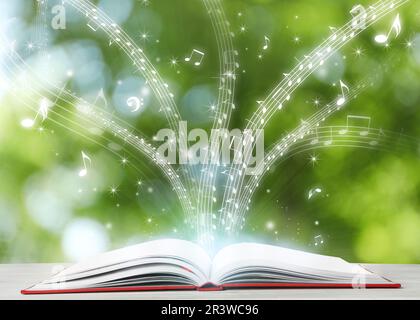 Musica che scorre dal libro. Simboli musicali che volano su tome su un tavolo di legno bianco su sfondo sfocato Foto Stock