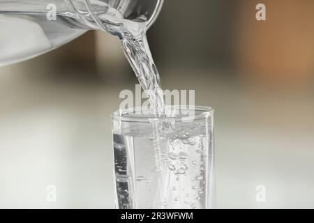 Versare l'acqua dalla caraffa nel vetro su sfondo sfocato, primo piano Foto Stock