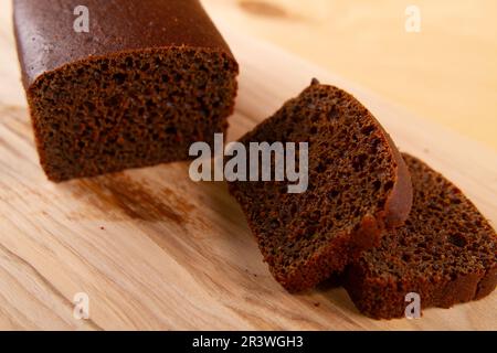 Pane scuro in forma di pagnotta e affettato posto su una superficie di legno beige chiaro. messa a fuoco selettiva Foto Stock