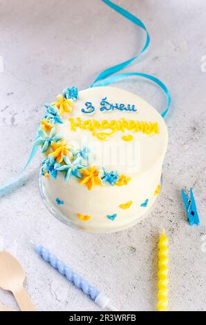 Torta bento alla moda con un'iscrizione blu-gialla in ucraino "buon compleanno" su sfondo chiaro. Torta di compleanno, torta Bento per due Ukrai Foto Stock