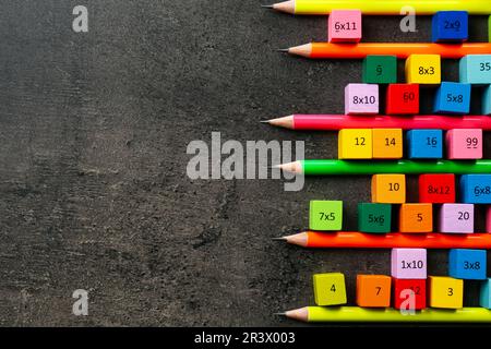 Molti cubi colorati con numeri, moltiplicazioni e matite su tavola grigio scuro, piatto. Spazio per il testo Foto Stock