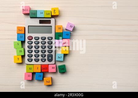 Cubi colorati con numeri e moltiplicazioni vicino calcolatrice su tavolo di legno bianco, piatto. Spazio per il testo Foto Stock