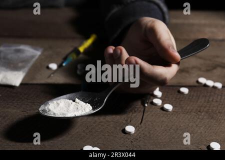 Uomo addicted che tiene il cucchiaio con le droghe al tavolo di legno, primo piano Foto Stock