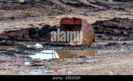 pala dell'escavatore rossa sdraiata su terreno fangoso Foto Stock