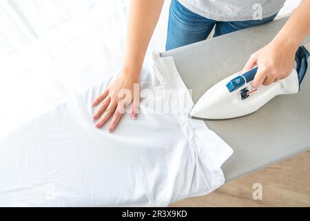 Le mani femminili stirare il colletto bianco della camicia sull'asse da stiro, vista dall'alto Foto Stock