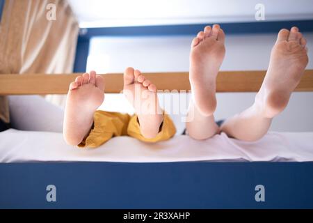 I piedi dei piccoli caucasici sono seduti sul letto a castello. Foto Stock