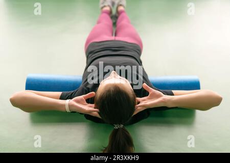 Femmina attraente facendo il rullo di schiuma rilassante esercizio la schiena e in posa di moderno luminoso centro fitness Foto Stock