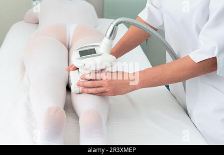 Donna in costume bianco speciale ottenere massaggio anti cellulite per le gambe in un salone termale. GPL, e trattamento di contornazione del corpo in clinica Foto Stock